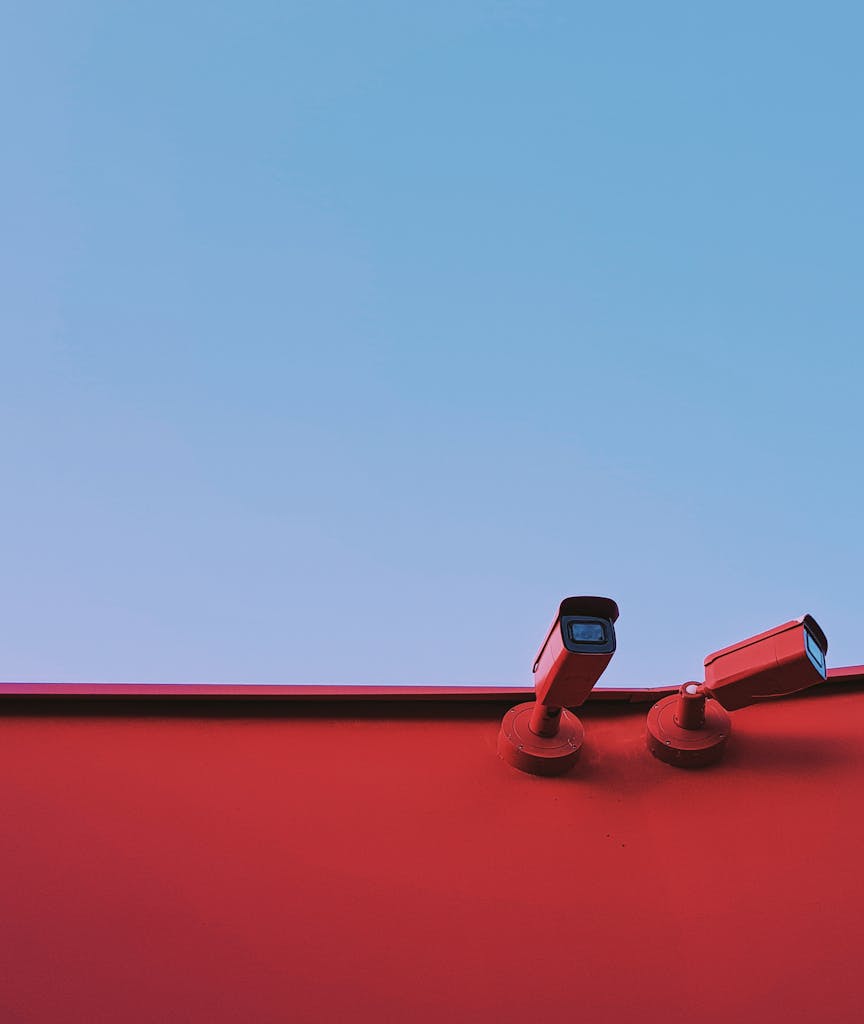 Low-angle shot of red CCTV cameras on a red wall with a clear blue sky background.