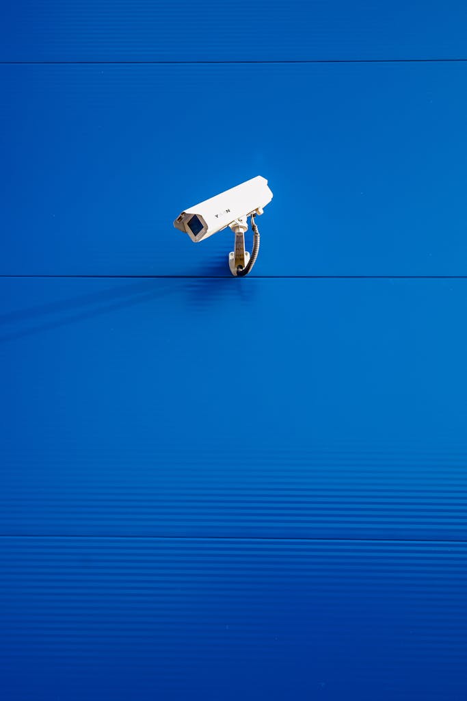 White security camera against a vibrant blue textured wall in a minimalist style.
